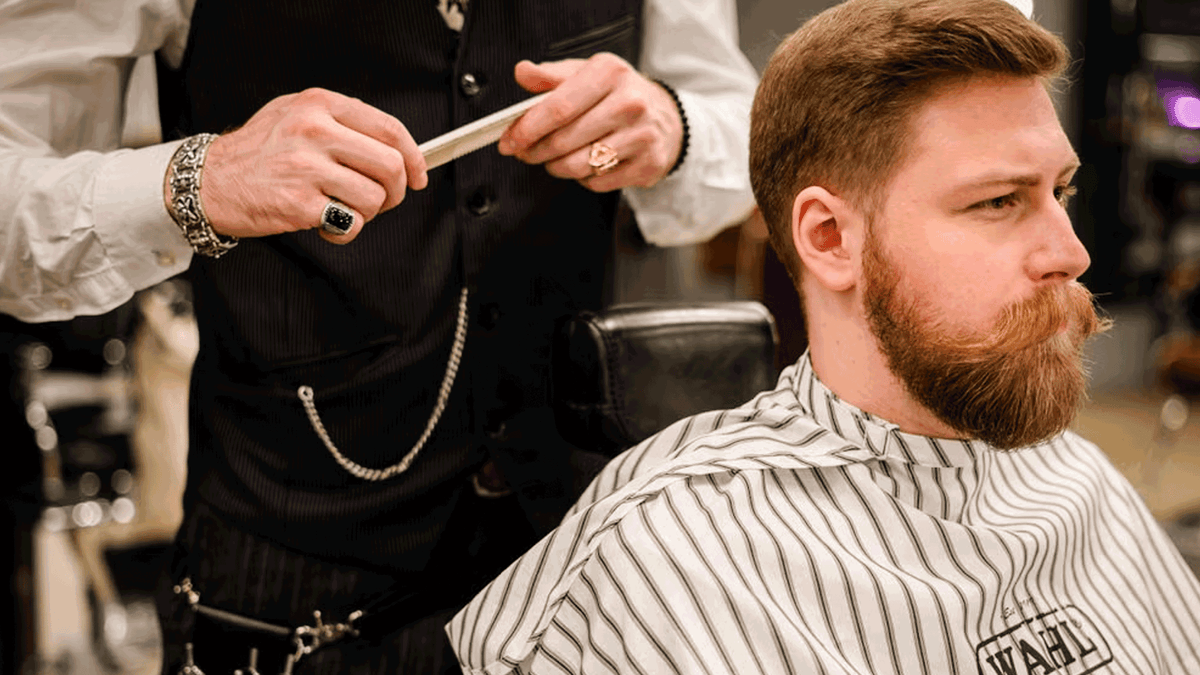 Bearded man at a barbershop having his full beard professionally trimmed and shaped.