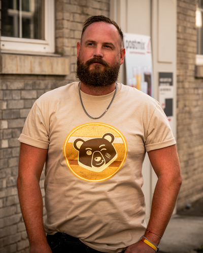 Bearded man wearing the desert beige Scruffy Cub Horizon T-shirt with a retro bear graphic